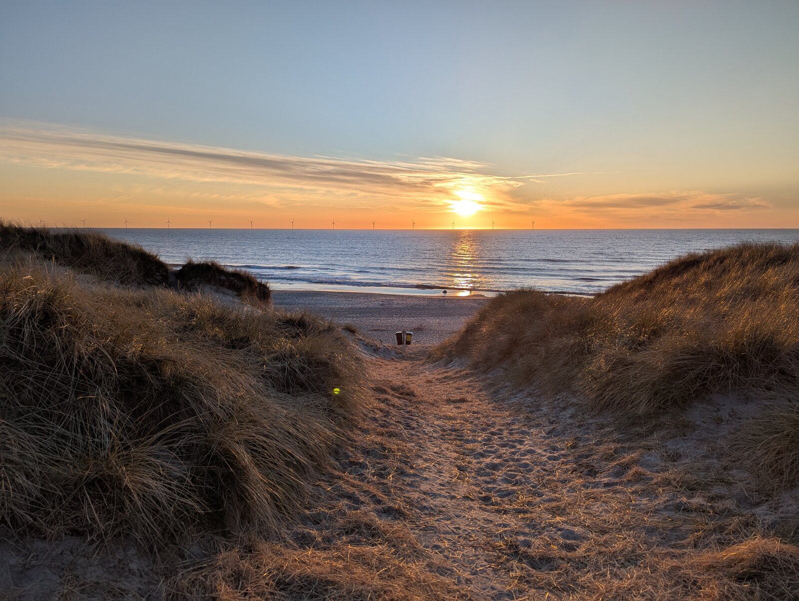 A sandy path between grassy dunes leading to the sea at sunset